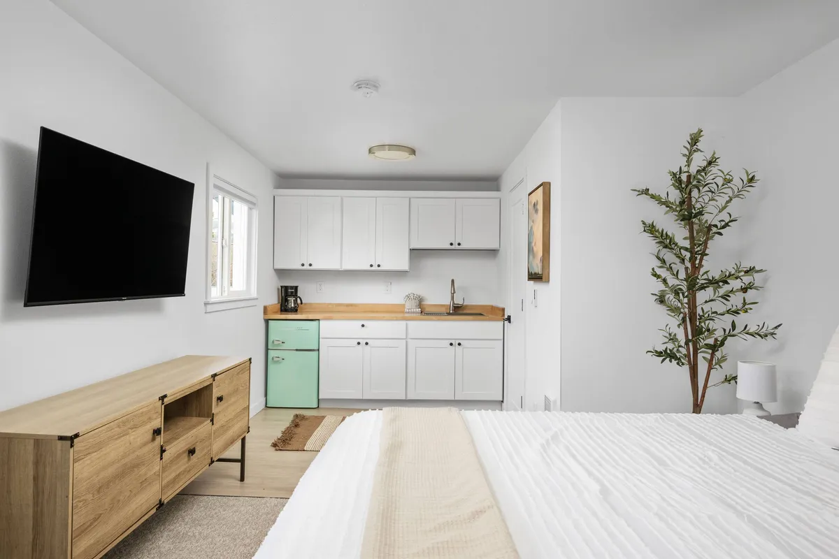 This image offers another angle on the living space, focusing on the green fridge, a wooden countertop, a TV, a plant, and part of the bed. The cozy ambiance is enhanced by touches of greenery and the suggestion of enjoying breakfast or coffee in bed, adding a layer of personal comfort and relaxation.