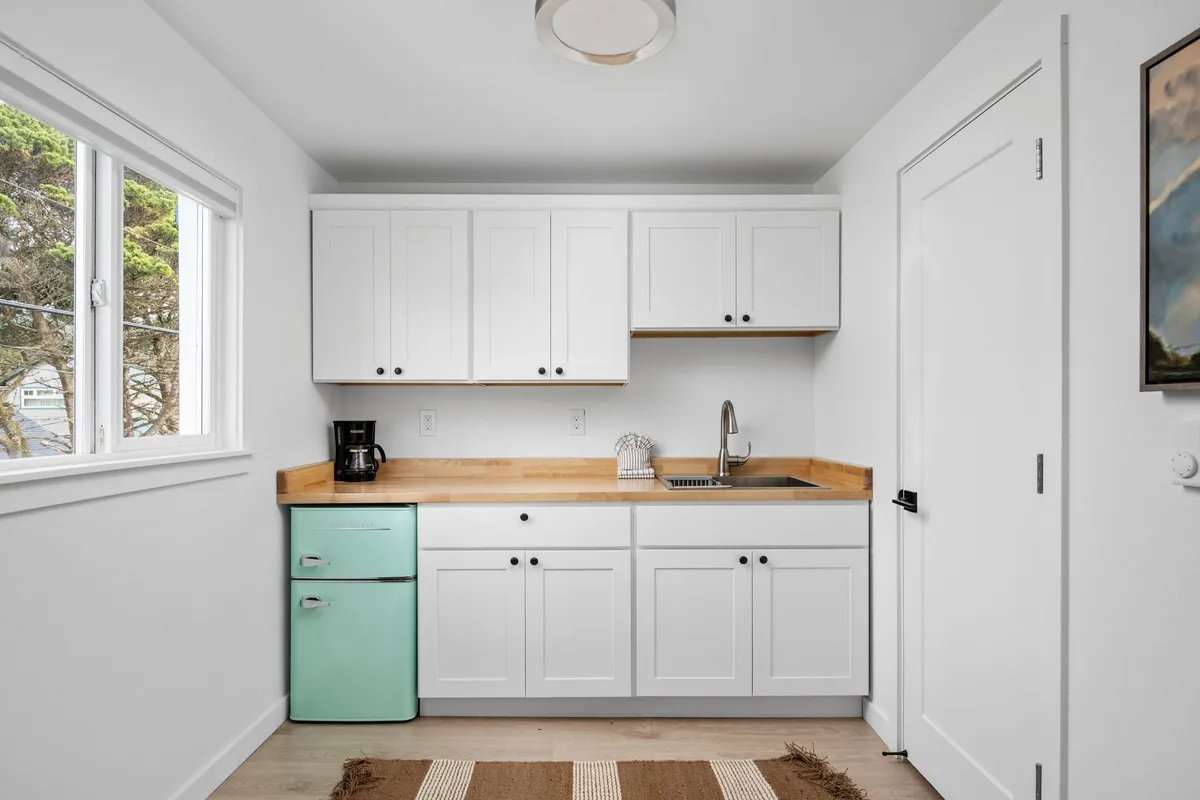 This image highlights a stylish kitchenette with a mint green refrigerator, wooden countertop, and a sink with a modern faucet. The scene feels lively and welcoming, suggesting activities like cooking, sharing a meal, or enjoying a cup of coffee. The well-designed space is both functional and inviting, capturing the heart of daily routines.