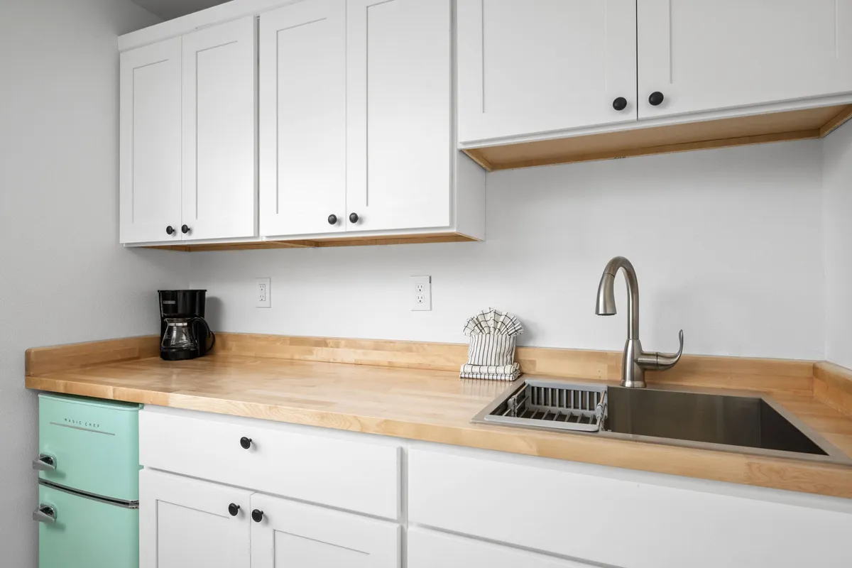 An inviting kitchenette interior featuring a mint green refrigerator, wooden countertops, a stainless steel sink, and a coffee maker. The space is ready for guests to prepare snacks or morning coffee, evoking the convenience of enjoying takeout from local restaurants or fresh-brewed coffee at home.